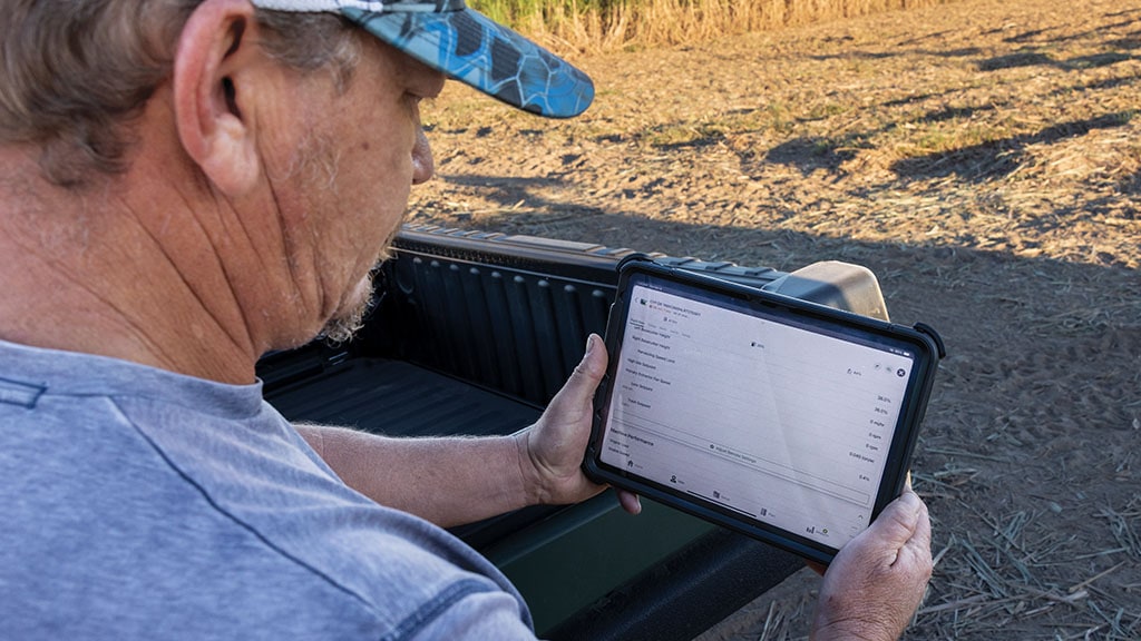 Close-up photo showing a farmer reviewing farm data on a tablet in a sugar cane field.