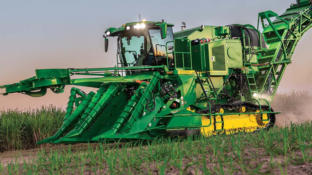 Photo showing a tracked CH Series Sugar Harvester harvesting with lights on at dusk.