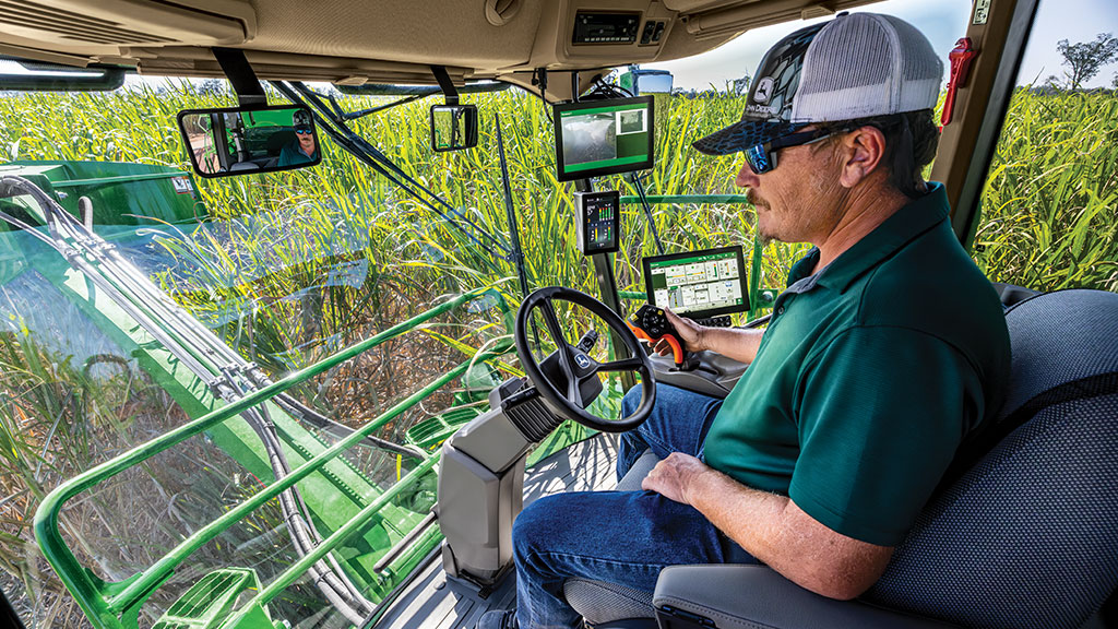 An in-cab, close-up photo of a farmer operating a CH Series Sugar Harvester, with standing crop visible through the front windows.