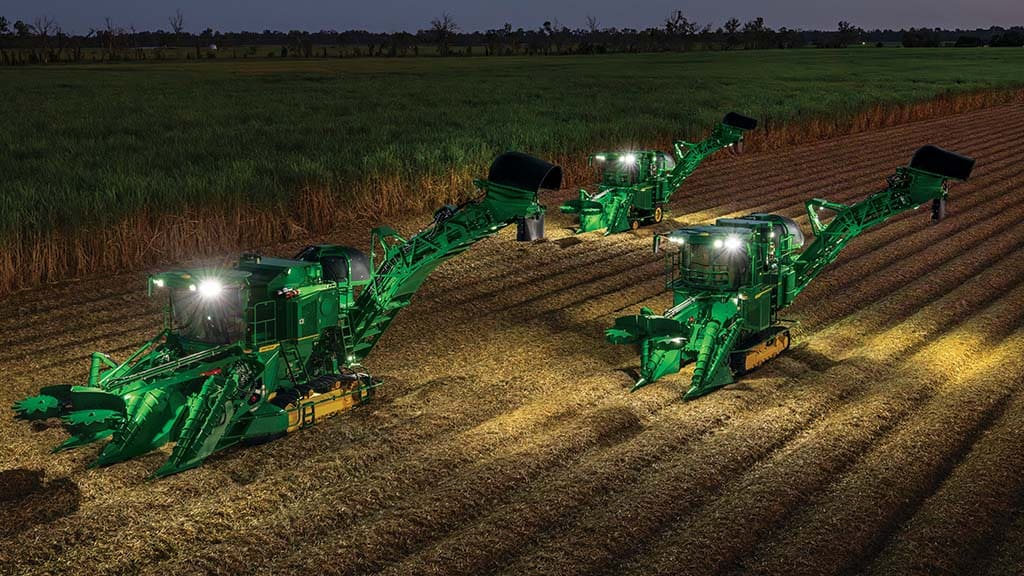 Photo showing three CH Series Sugar Harvesters working with lights in a partially-harvested sugar cane field at night.