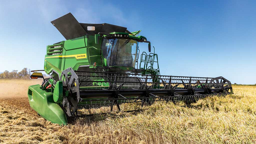 John Deere X9 1000 combine with draper and reel header facing right while combining rice