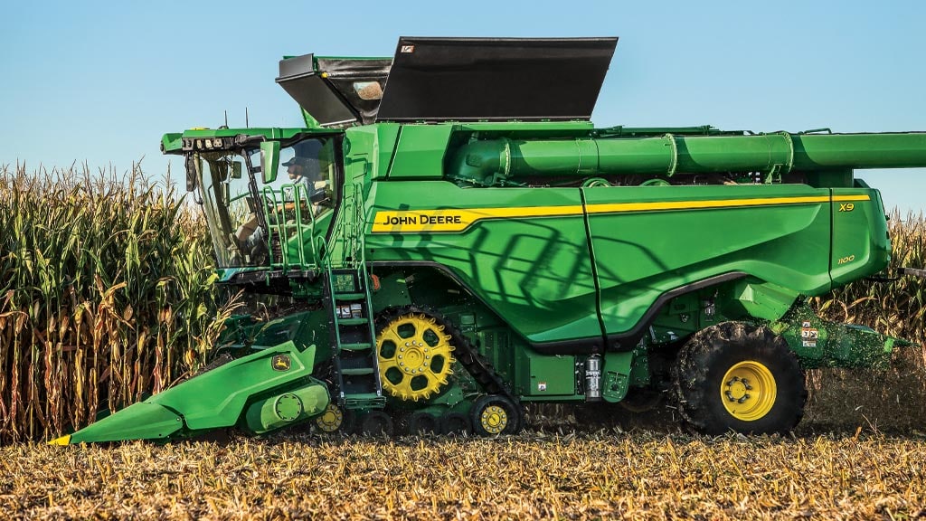 Photo of a John Deere X9 Combine with front tracks, harvesting corn with a corn head