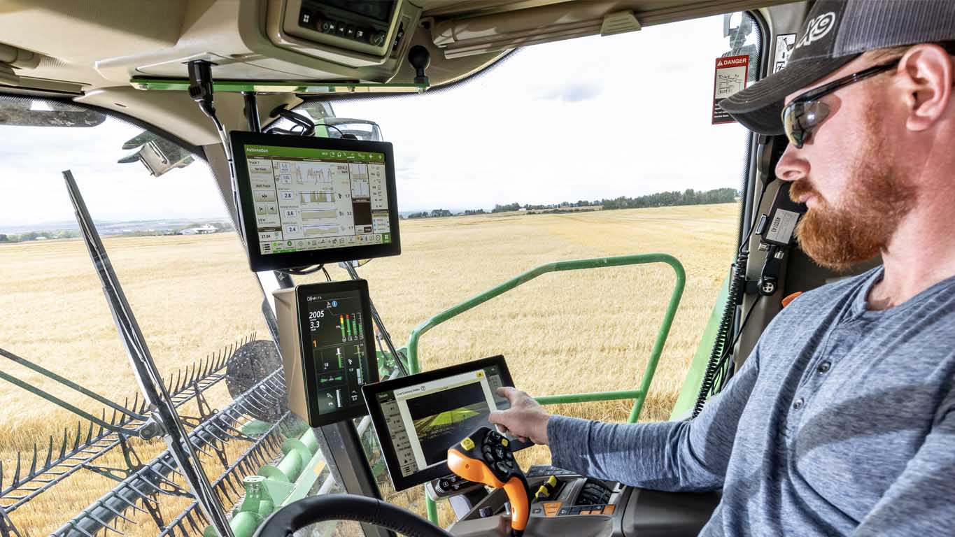 In-cab photo of a farmer in a John Deere Combine, adjusting his Harvest Settings Automation run page on a G5Plus CommandCenter™ Display