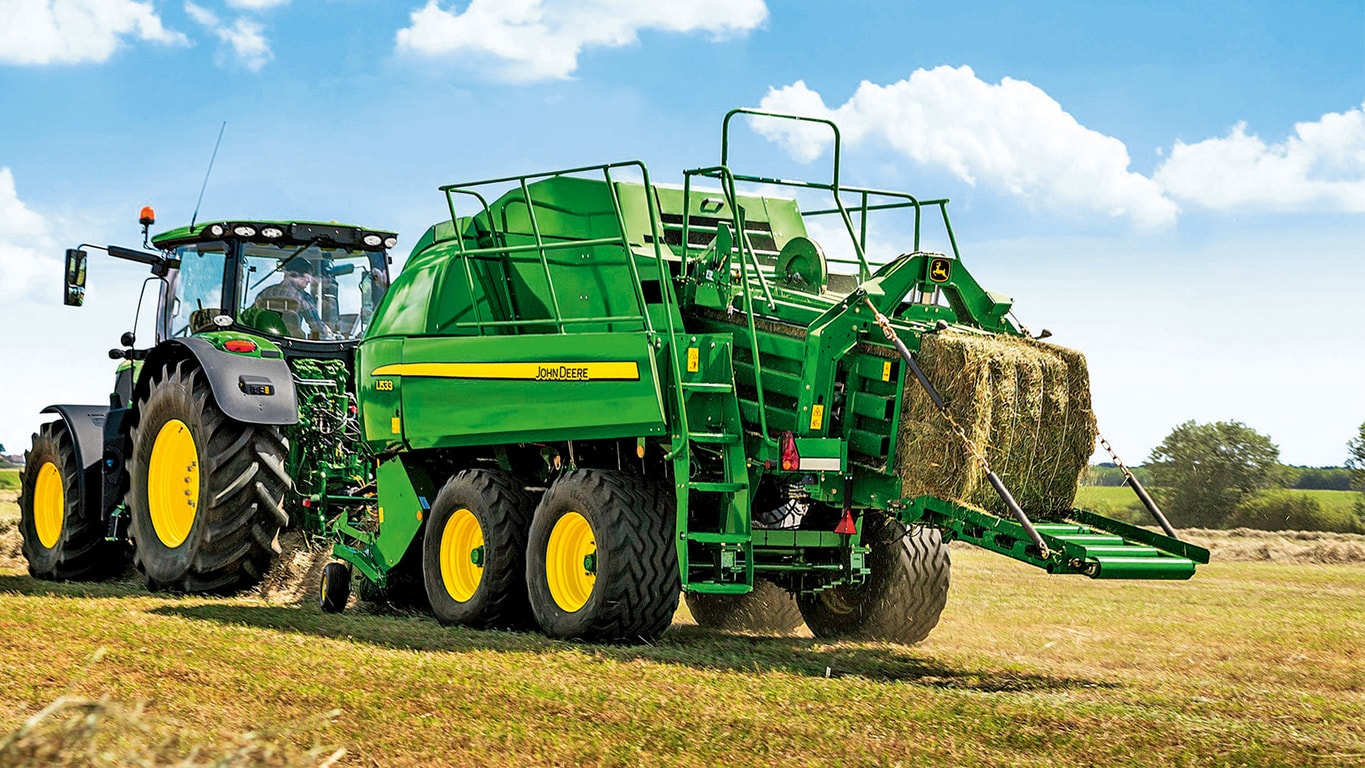 a John&nbsp;Deere tractor towing equipment carrying hay through a field