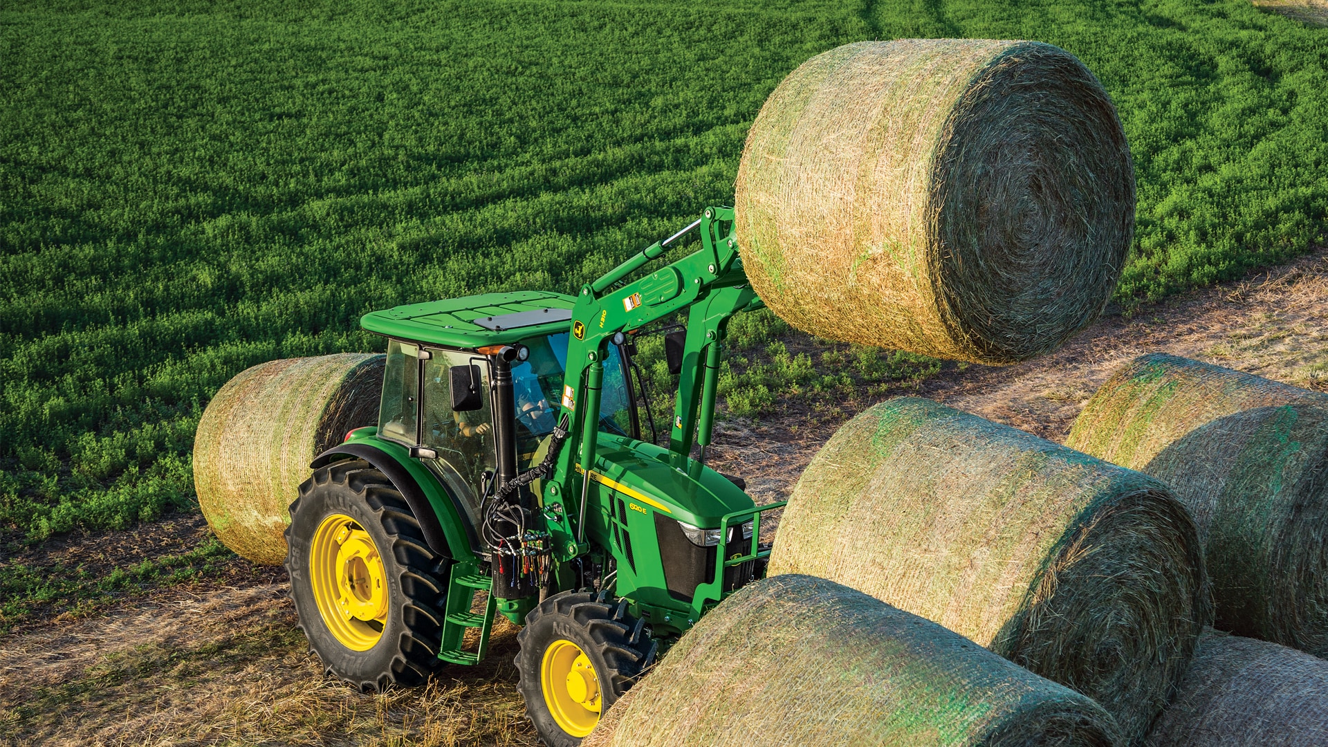 John Deere tractor handling a round hay bale