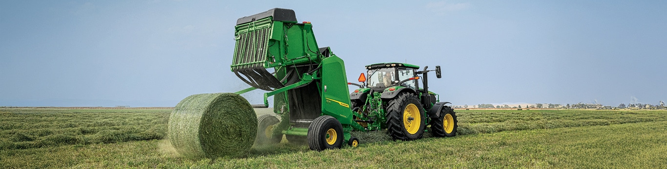 Tractor pulling baler that's ejecting a bale of hay.