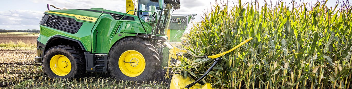 John Deere tractor with green-yellow header harvesting corn in a field.