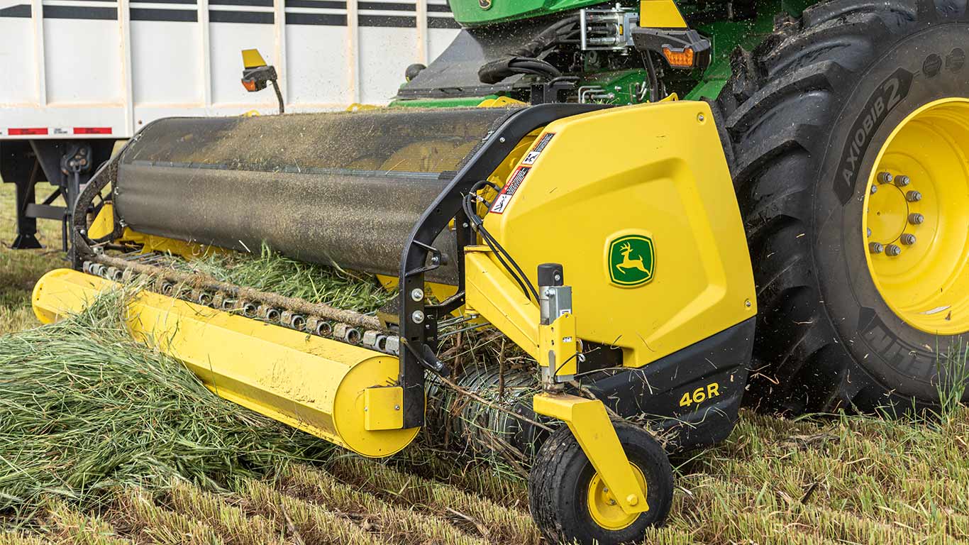 John Deere 46R baler on green tractor collecting cut grass in a field.