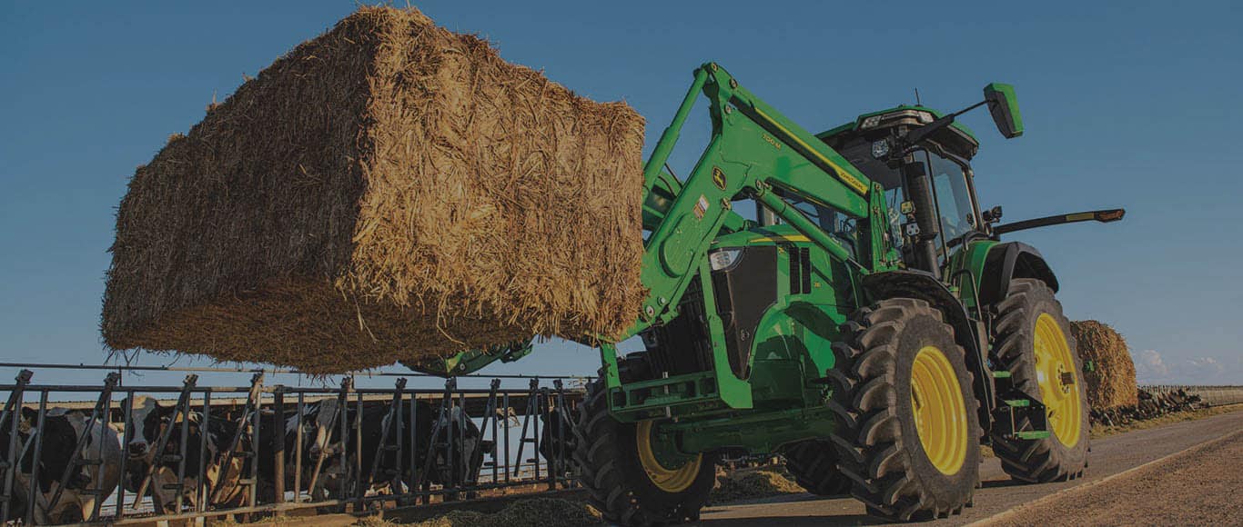 Image of tractor with loader and forks carrying hay bale