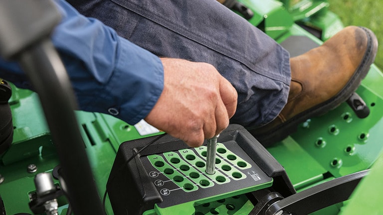 A person in a work vest driving a green zero-turn mower out of the back of a trailer.