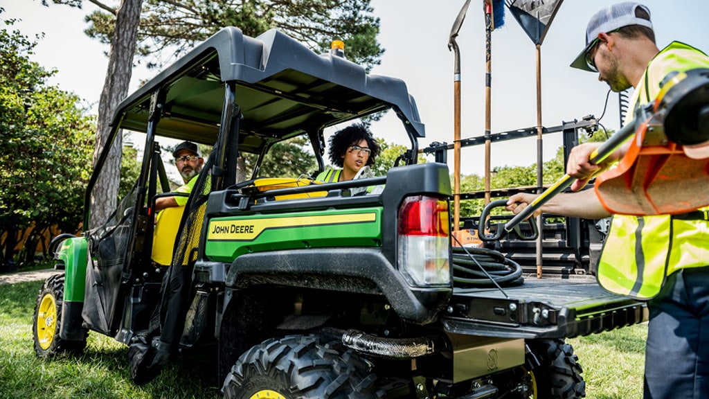 Man putting a weedwacker into the cargo box of a Gator Utility Vehicle