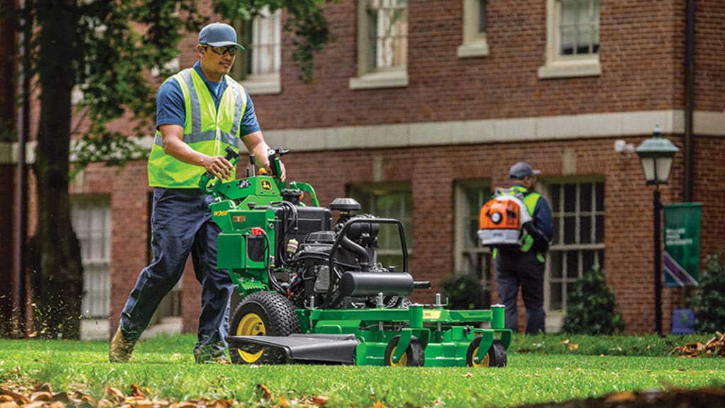 man using a quiktrak mower on a campus lawn