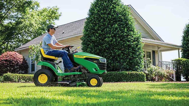 Right-side view of a person driving a green riding mower with grass clippings coming out the side.