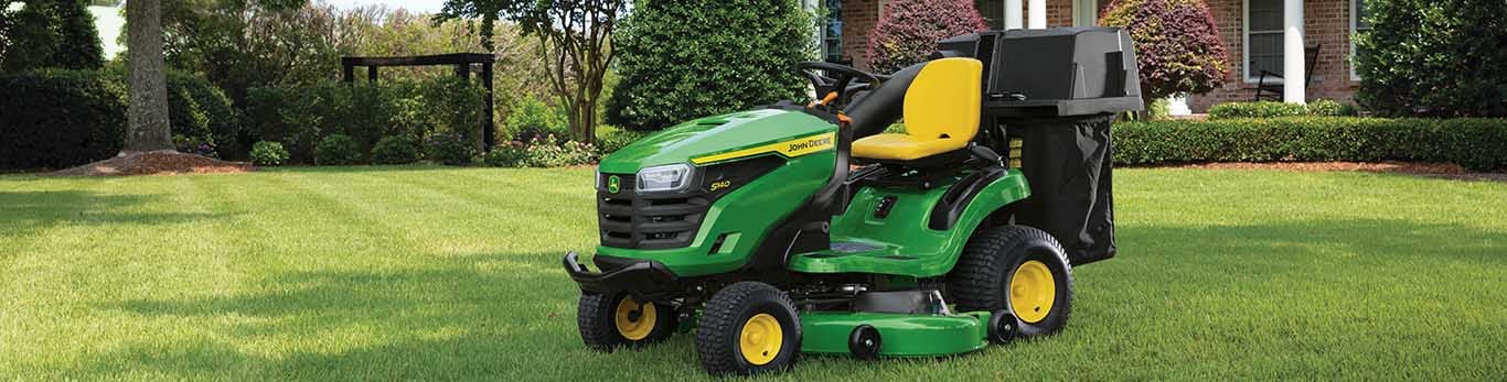A green riding mower with a bagging attachment sitting on a well-kept lawn.