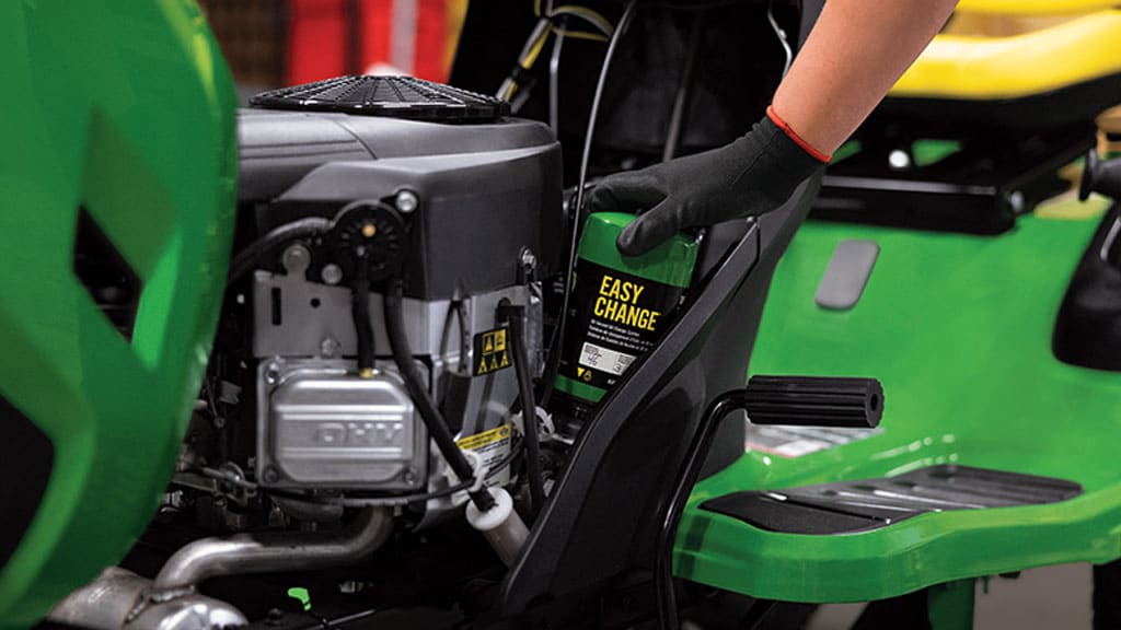 Close-up of a person's hand inserting an Easy Change oil canister into a riding mower's engine.