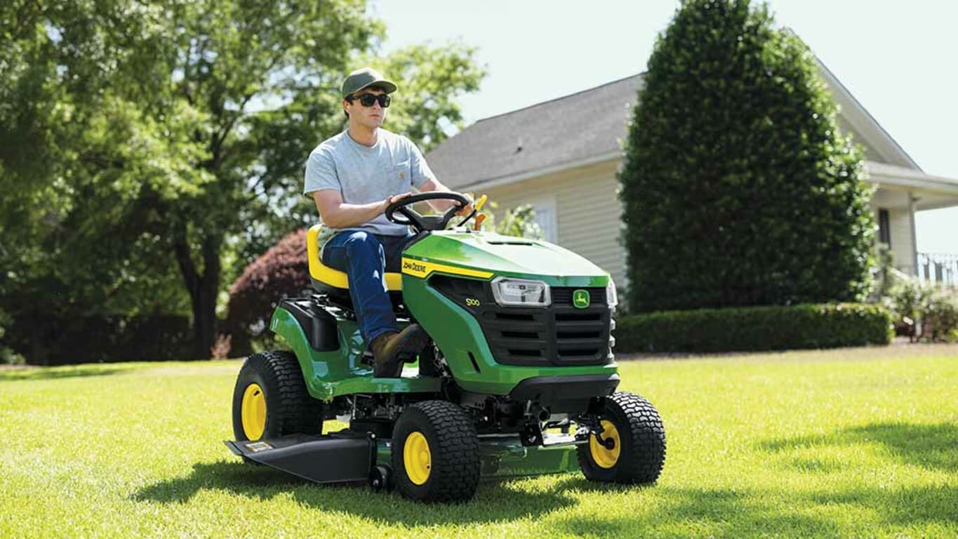 Close-up of a person driving a green riding mower over a flat even lawn.