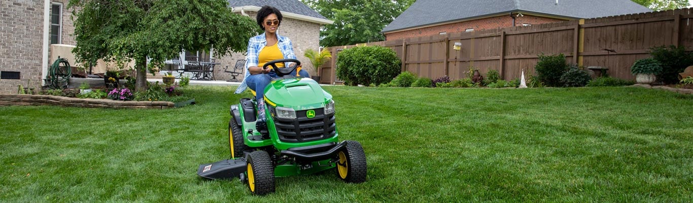woman driving 100 series lawn tractor in yard