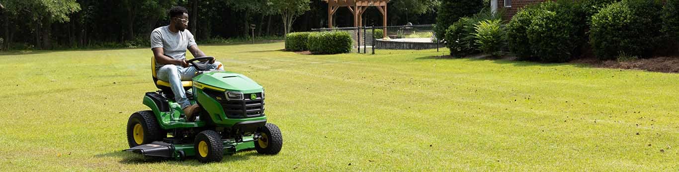 A person driving a green riding mower over a large lawn of short even grass.