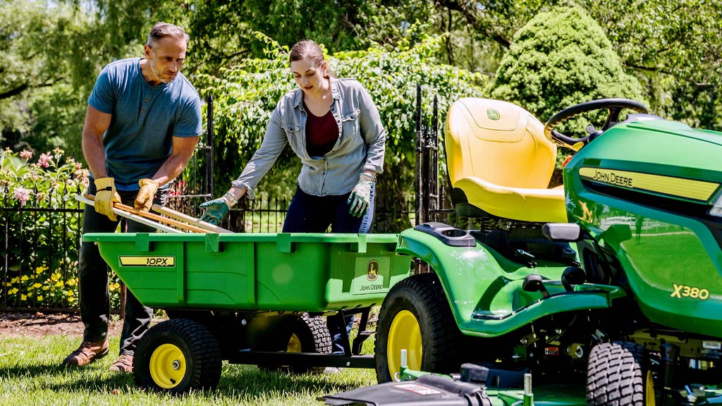 woman and man on a X300 lawn mower with man unloading top soil bags from cart