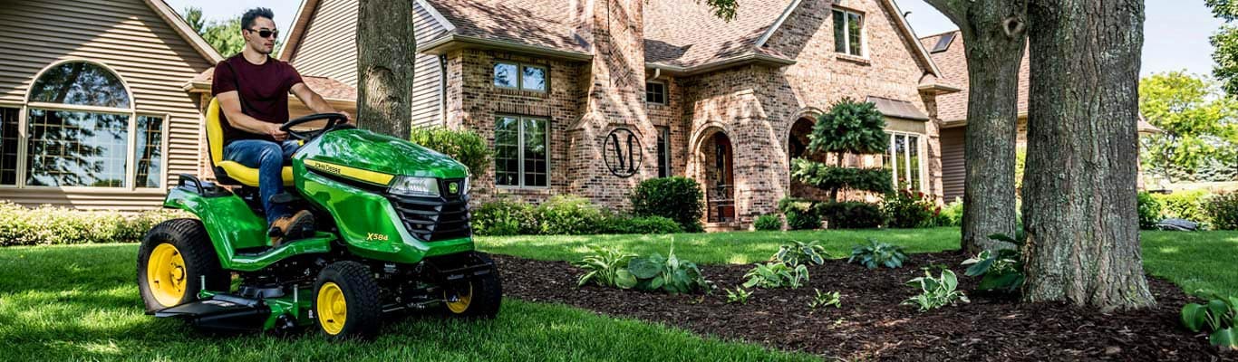  2024 John Deere X504 Lawn Tractor mowing around a garden and large tree