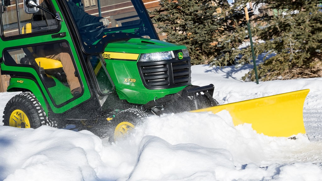 image of snow plow attachment on lawn mower plowing snow