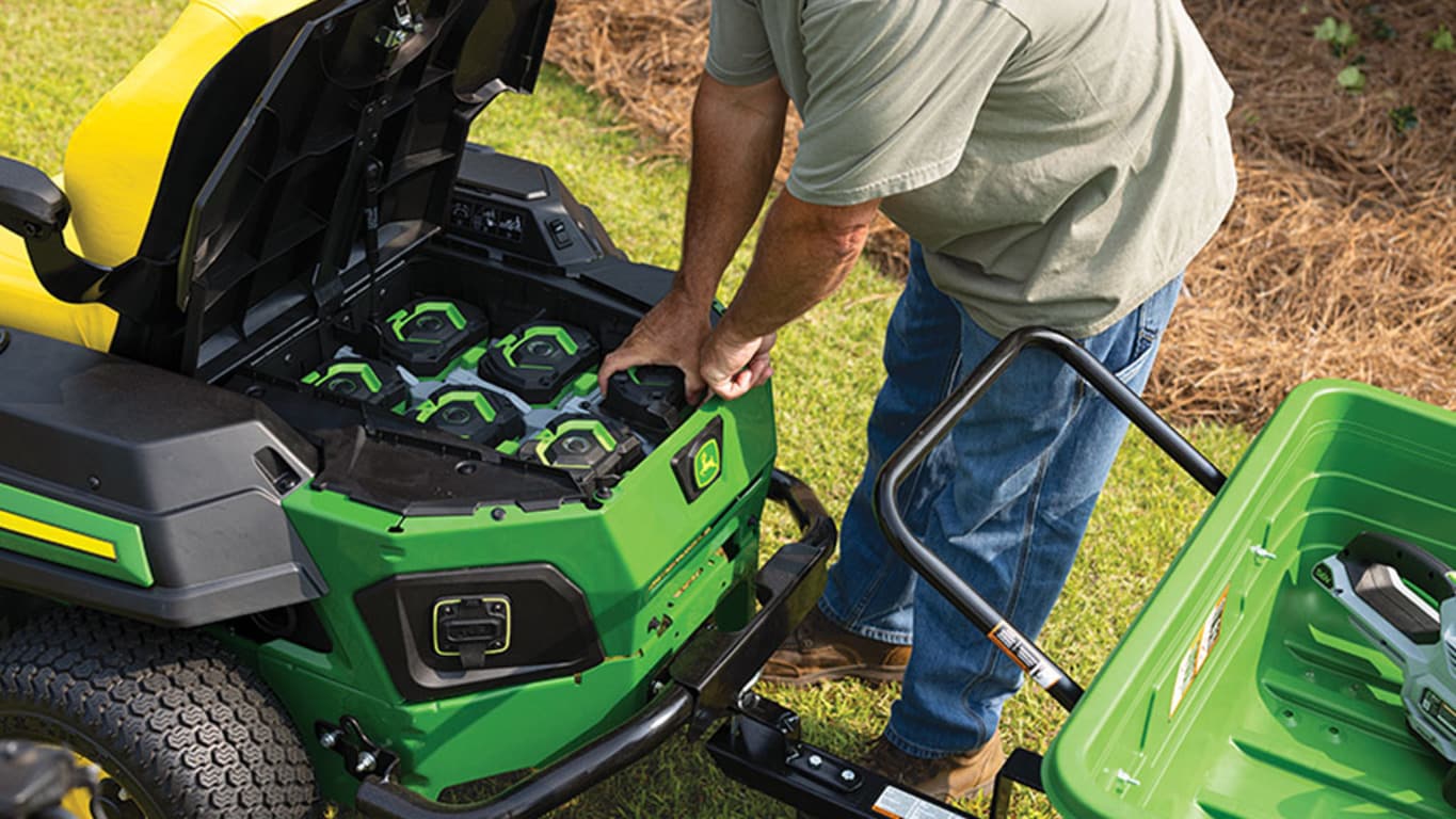 A person reaching into the battery compartment of an electric zero-turn mower and pulling out a battery.