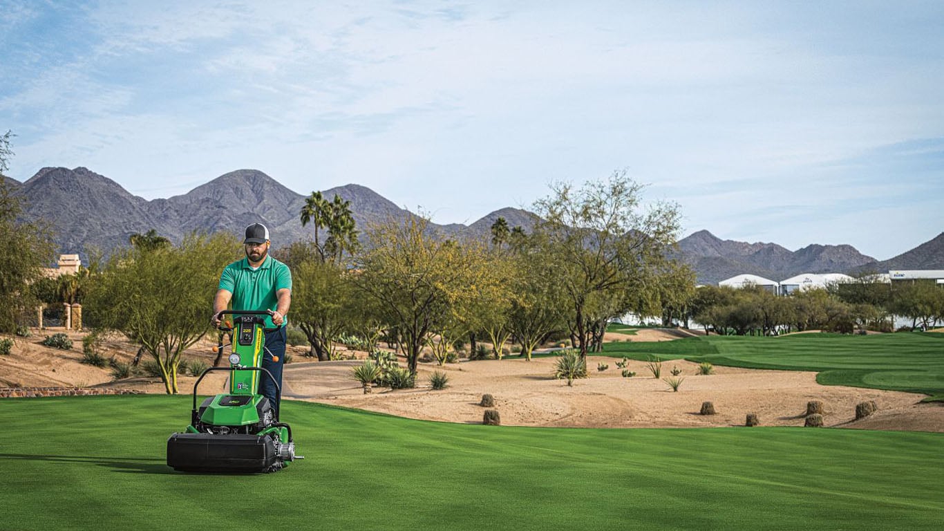 Worker operating 225 E-Cut Electric Walk Greens Mower on golf turf with desert mountain landscape