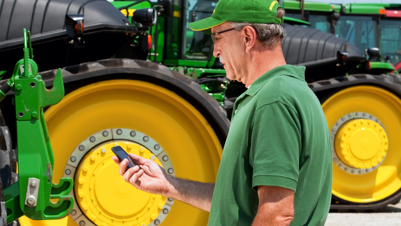 Image of a man looking at a cell phone in front of at tractor
