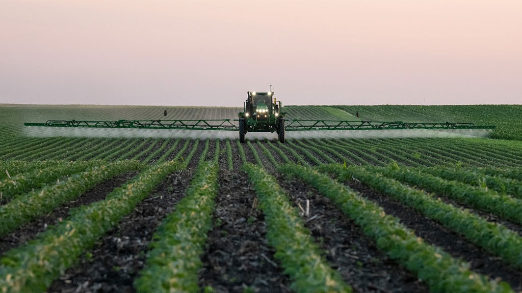 John Deere 408R 132 feet long sprayer spraying a large field of crops