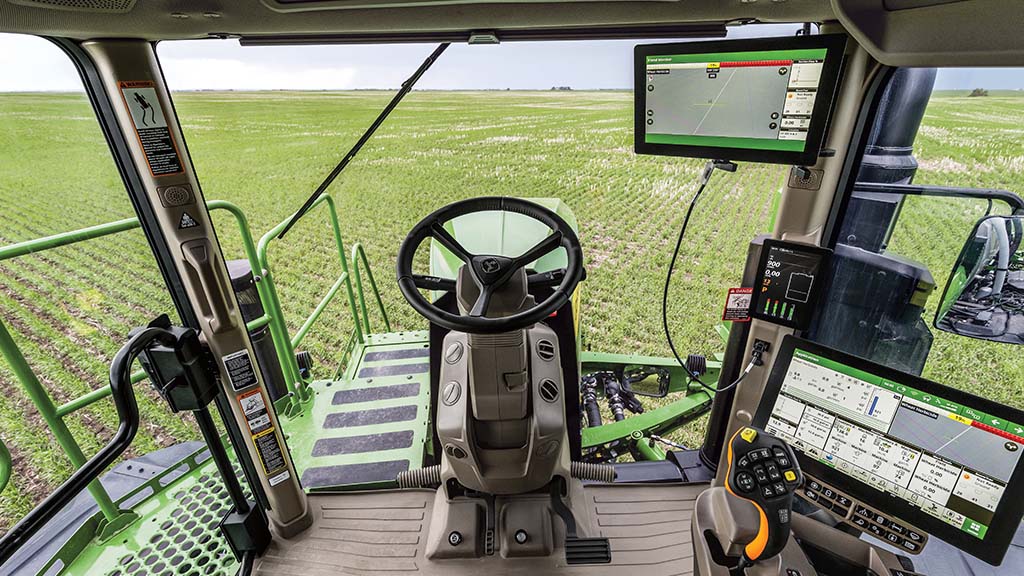 View from inside a John Deere self-propelled sprayer cab overlooking a field.