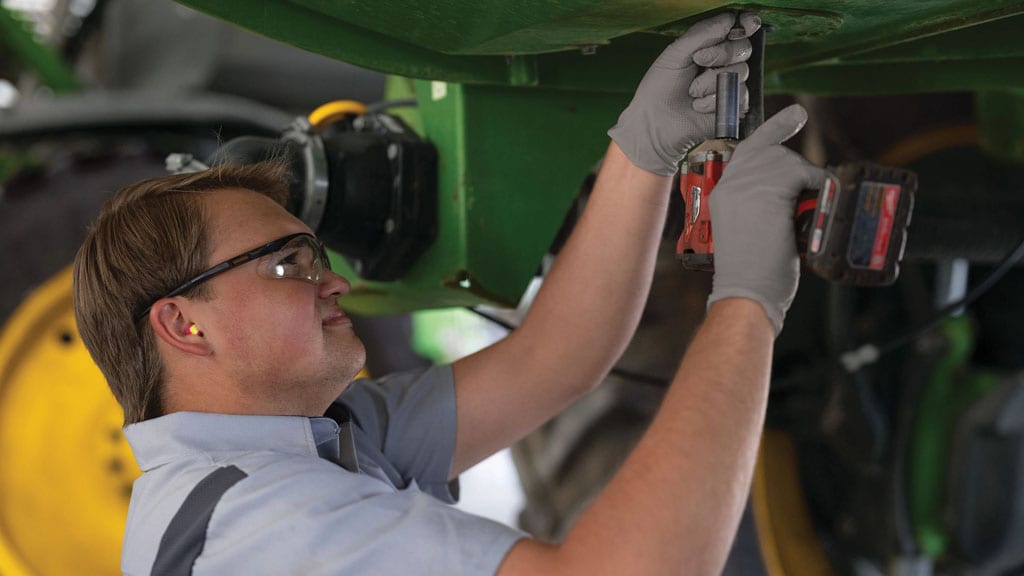 John Deere repair specialist working under a John Deere Self-Propelled Sprayer.