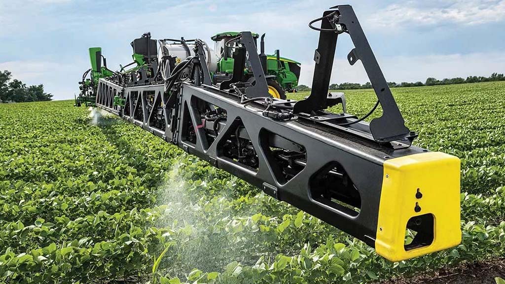Photograph shot from a 3/4 angle showing a See & SprayTM-equipped John Deere Sprayer making an application pass in row crops.