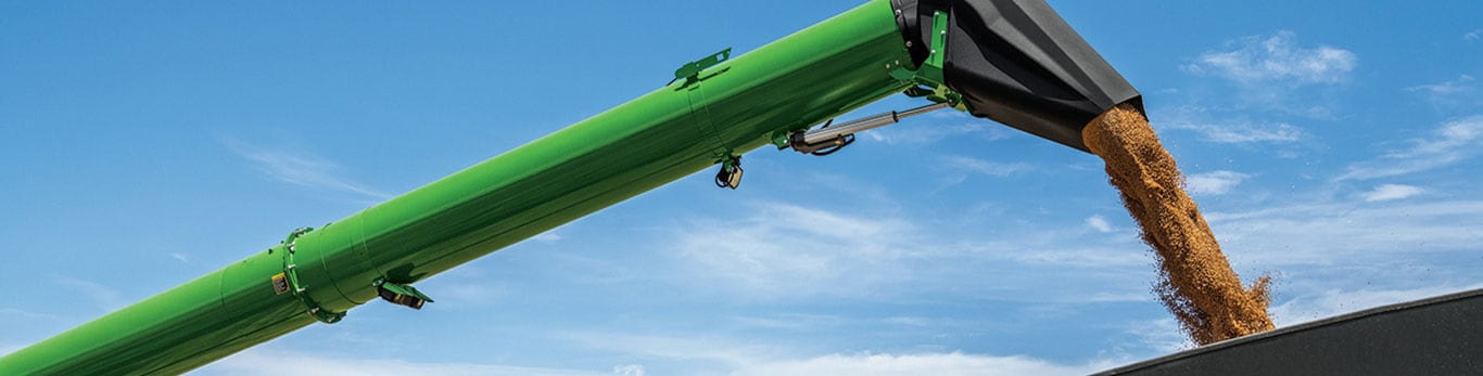 A green agricultural machine pouring golden corn into a truck on a clear, sunny day, with fields stretching in the background.