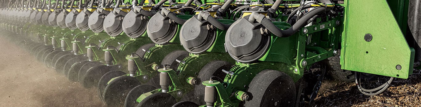 Close-up of a precision agricultural planter, featuring multiple planting units and rows in a dusty field setting.