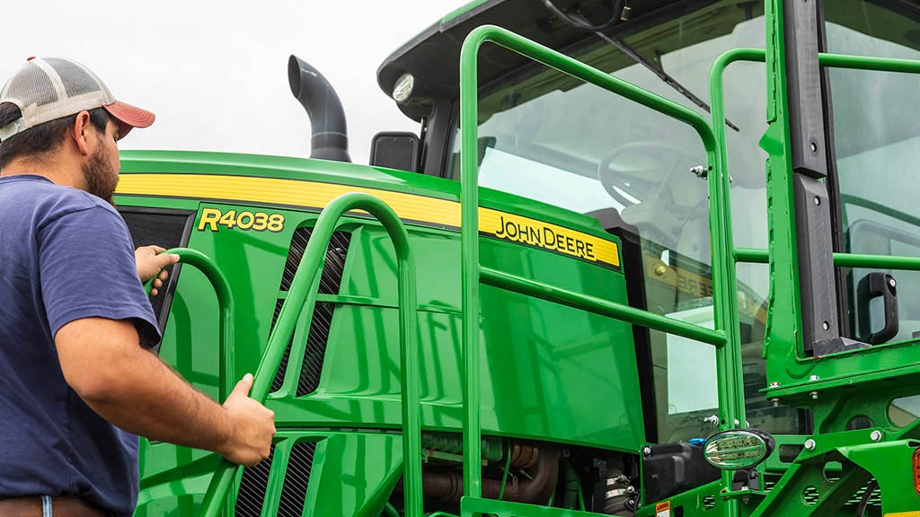 A farmer climbing onto a John Deere 44038 Sprayer.