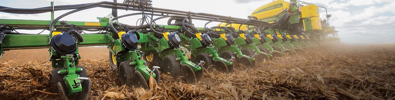 Close-up of a green John Deere planter's seed discs, working in tilled soil with plant residue, ready for planting.