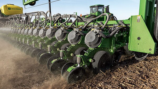 Close-up of a planter with large rubber wheels, preparing soil, generating dust in a field under bright sunlight.