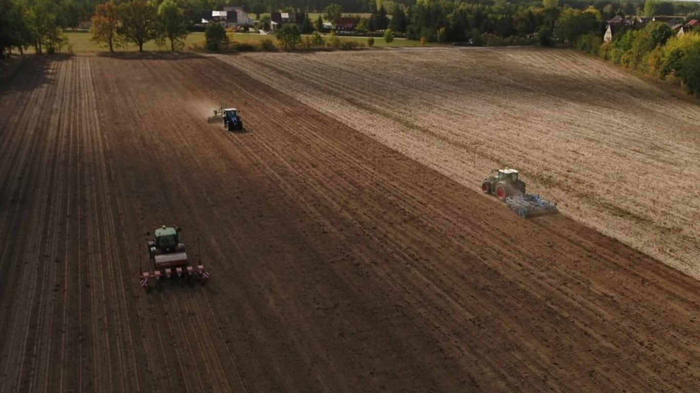 birds-eye view of three green tractors preparing a large crop field
