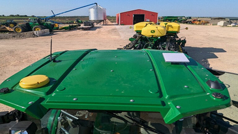 Vista desde arriba de un tractor John Deere, mostrando su techo, antena y equipo de navegación.
