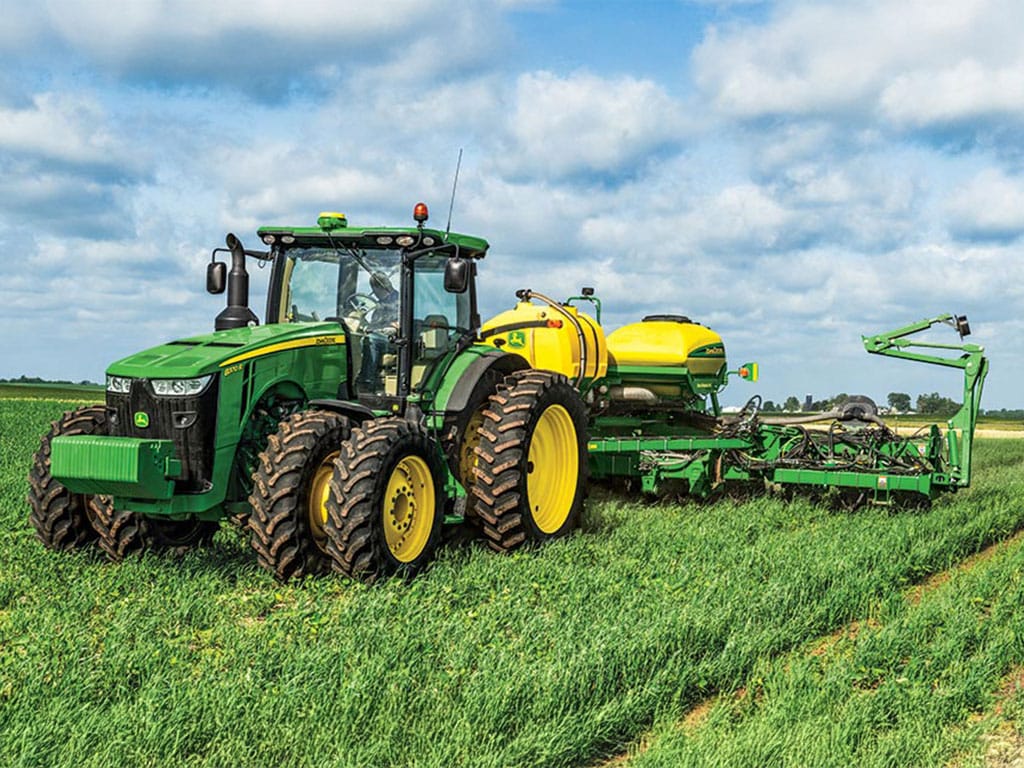 Green tractor with yellow wheels pulls a yellow-green implement across a field.