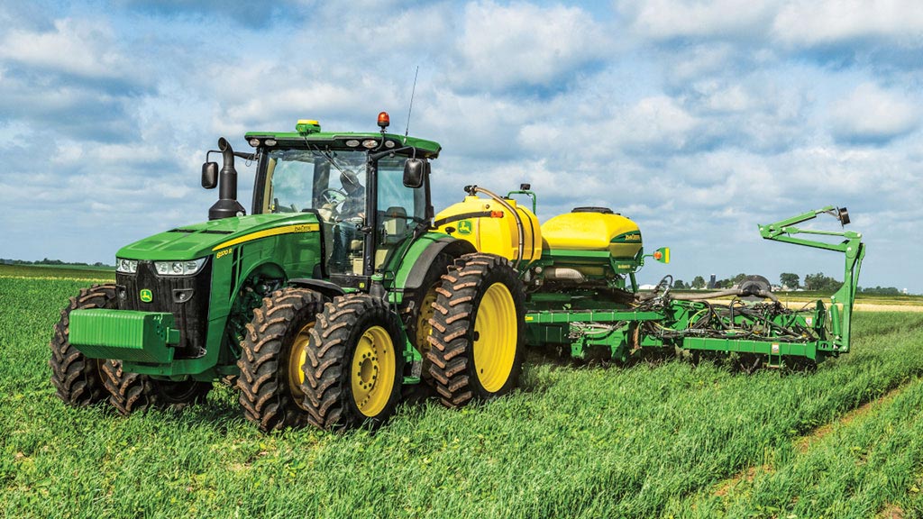 Tracked tractor pulling tillage equipment across a harvested field under clear sky.