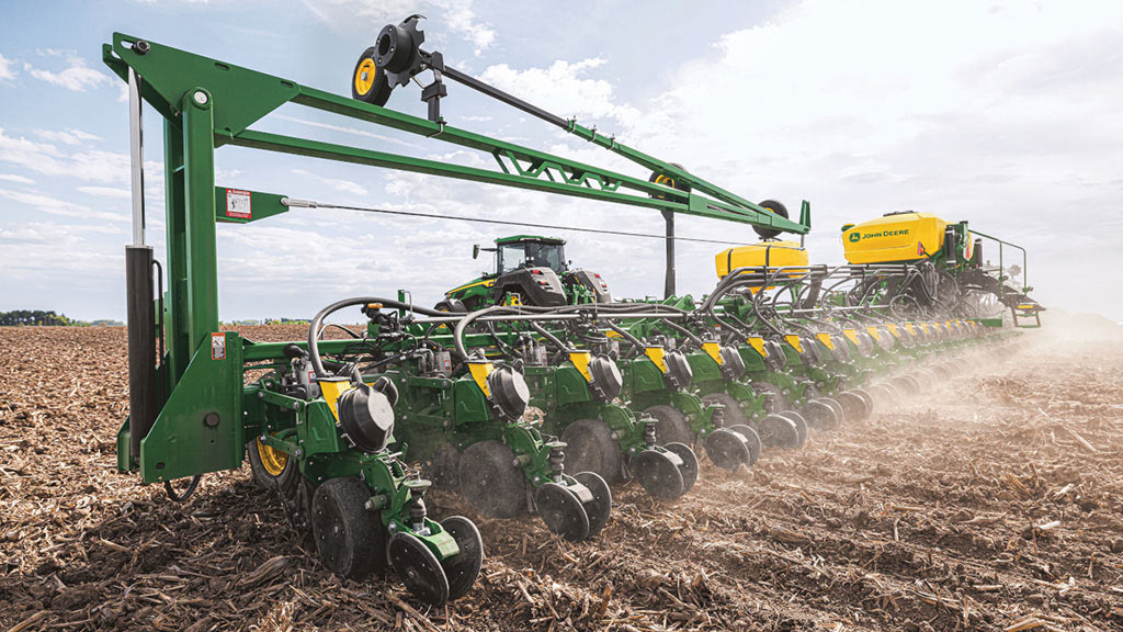 John Deere multi-row planter working across a crop residue field, with a tractor visible in the background. John Deere multi-row planter working across a crop residue field, with a tractor visible in the background.