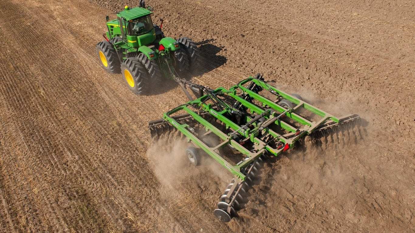 An aerial view of a green tractor pulling tillage attachment in a field.
