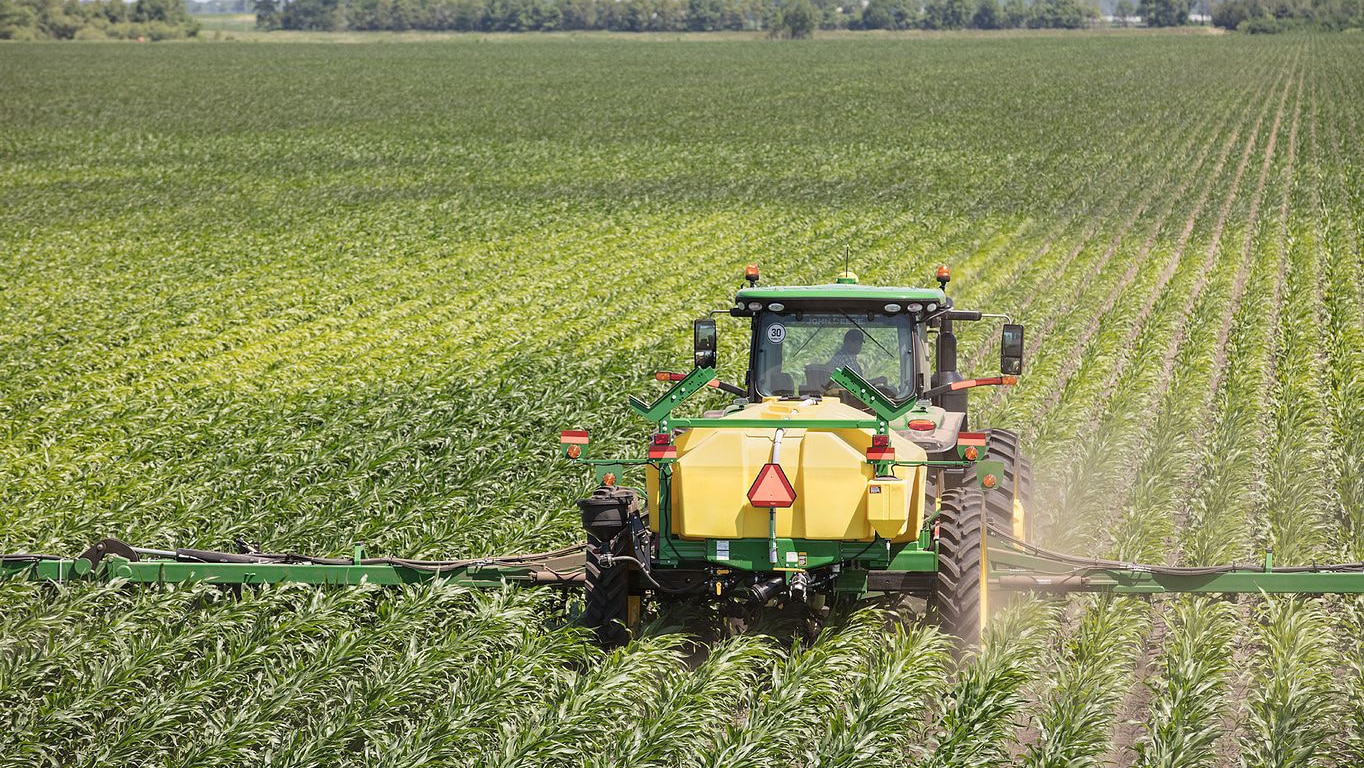 A 2530L nutrient applicator is operating in a field, showcasing its long frame and multiple row units designed for liquid fertilizer application.
