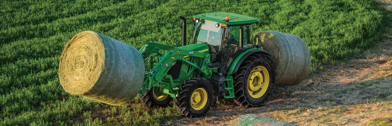 6M Tractor transporting a large round bale with a front spear.