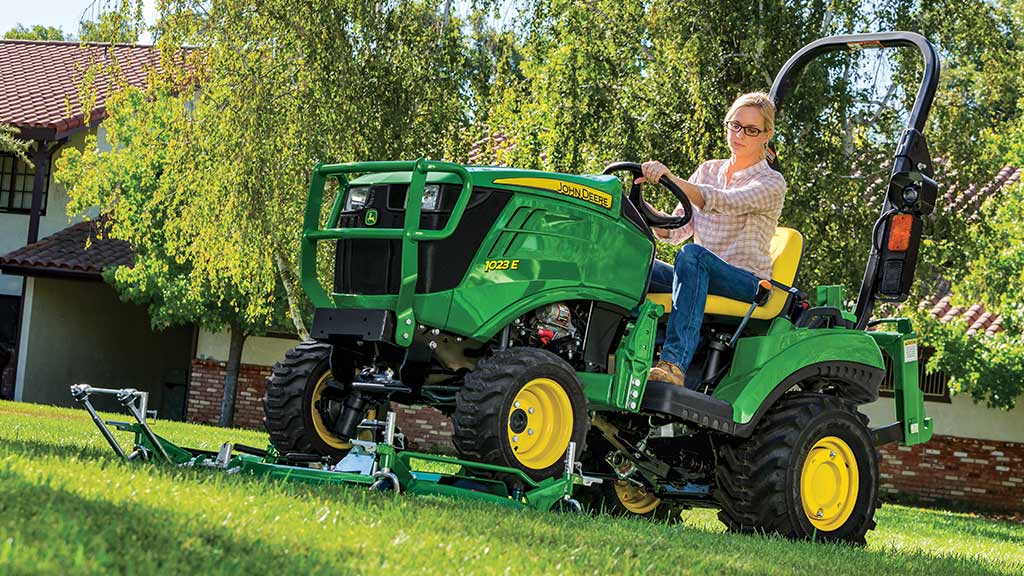 A green compact tractor on an AutoConnect mid-mount mower deck cutting a lawn.