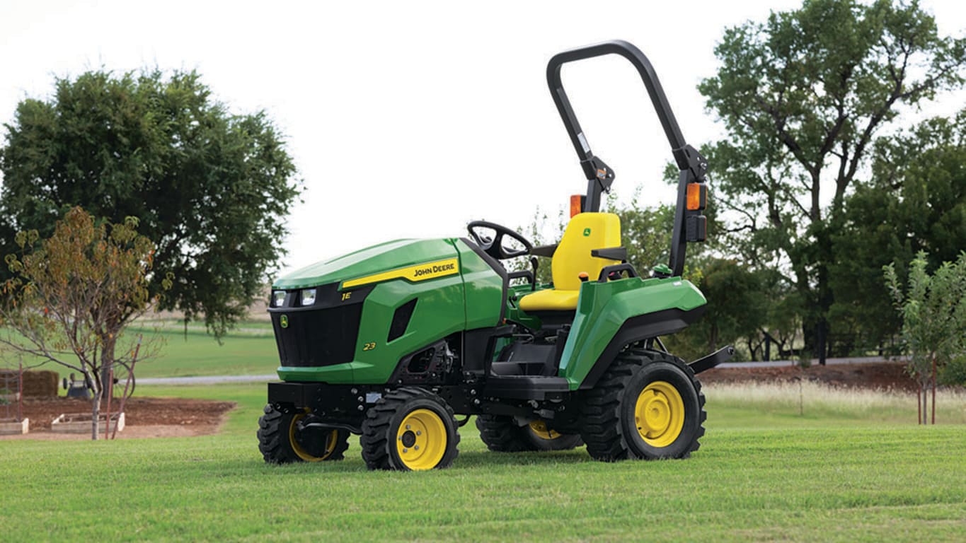 A flat open field has a green compact tractor with a yellow seat resting on it.