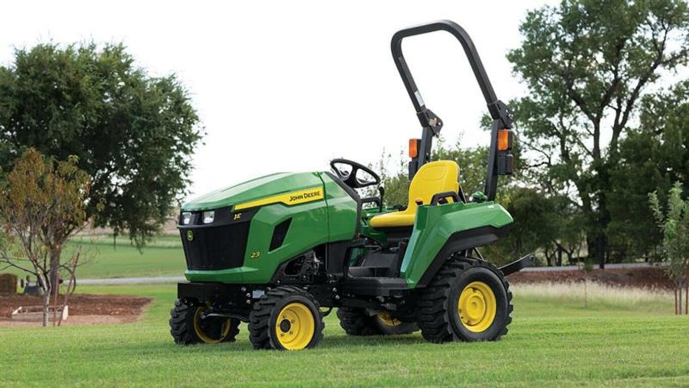 A flat open field has a green compact tractor with a yellow seat resting on it.