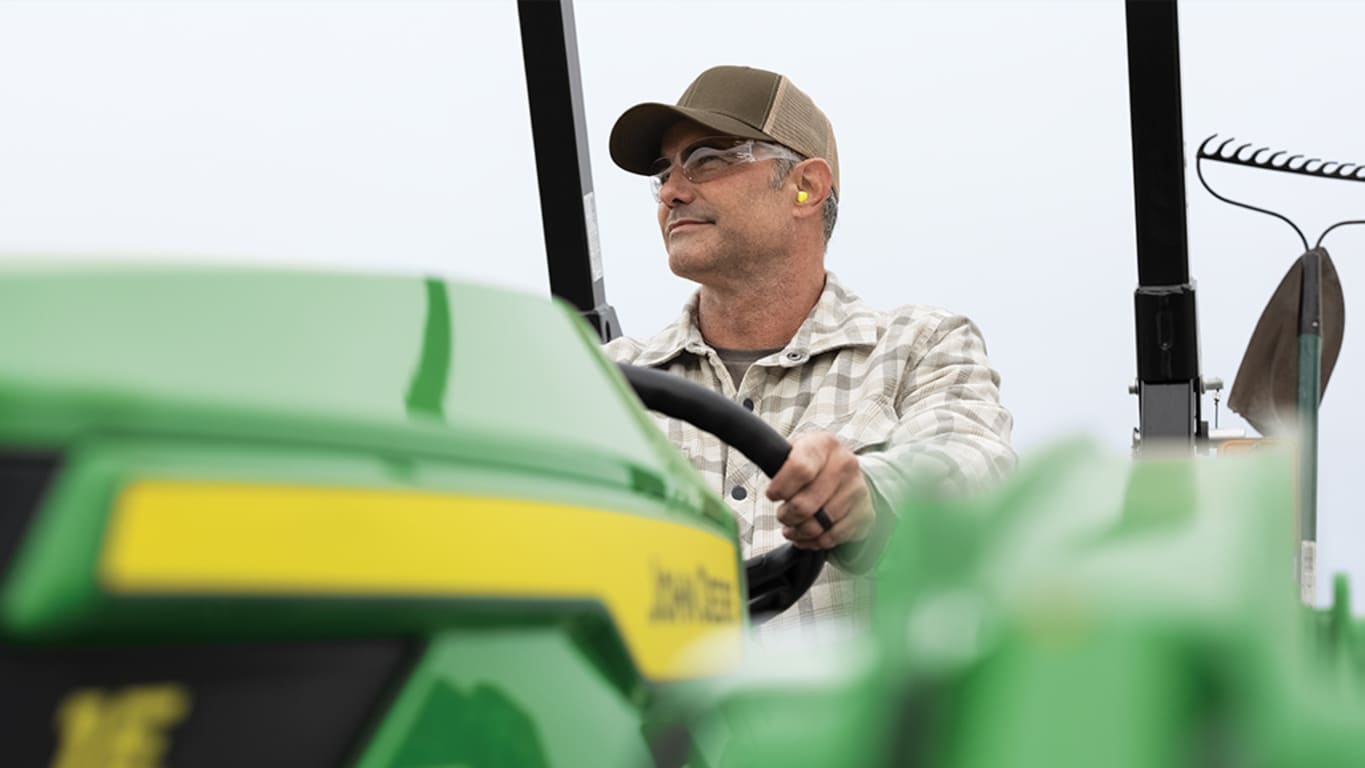 Close up of a person smiling atop an out-of-focus green compact tractor.