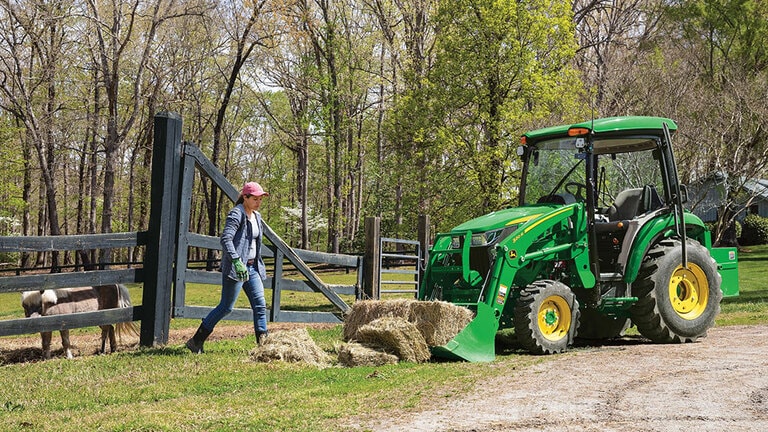 person in a field walking near a  3046r with hay bales in the loader